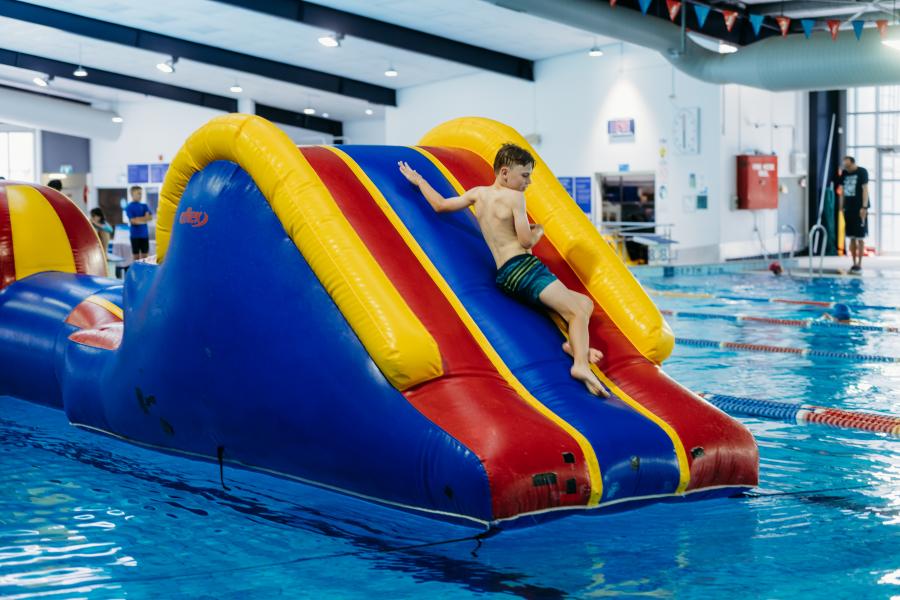 Young boy sliding down the end of the large inflatable at Aqualink Nunawading
